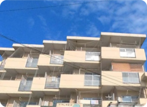 介護施設の建物外観。複数階建ての白とオレンジ色のタイル張り外壁で、各階にバルコニーが配置されている。