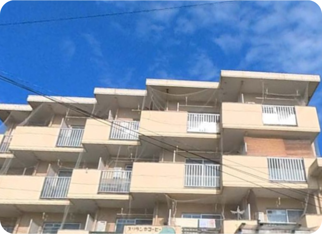 クリーム色の4階建て集合住宅の外観。複数のバルコニーと白いフェンスが見える。